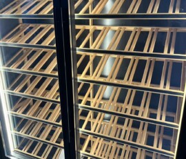 Full-height angled timber wine racking inside illuminated glass-door display cabinet