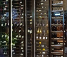 Full-height climate-controlled wine wall installed in a restaurant, bronze frame with glass doors and rolling access ladder